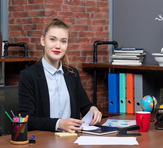 Top view of young female office worker sitting at her desk and posing for camera
